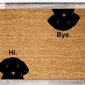 Puede incluir: Una alfombra de coco marrón con siluetas de perros negros y las palabras "Hi." y "Bye."