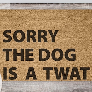 Puede incluir: Una alfombra de bienvenida marrón con el texto "SORRY THE DOG IS A TWAT" en letras negras.