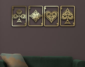 May include: Four gold metal wall decor pieces in the shape of playing card suits: clubs, diamonds, hearts, and spades. The pieces are arranged horizontally on a dark gray wall above a green sofa.