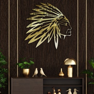 Könnte beinhalten: Eine goldene Wanddekoration aus Metall, die einen indianischen Häuptling mit Kopfbedeckung zeigt. Die Dekoration ist an einer dunkelbraunen Wand mit goldenen Verzierungen angebracht. Die Dekoration befindet sich über einem dunkelbraunen Holzkasten mit goldenen Akzenten. Der Kasten ist mit goldenen Dekorationsgegenständen geschmückt, darunter eine Lampe, Vasen und Figuren.