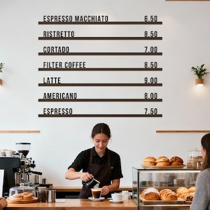 May include: A coffee shop interior with a wooden counter and a menu board listing coffee drinks and prices. A barista pours coffee into a cup. Pastries are displayed in a glass case. Customers are waiting.
