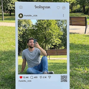 Könnte beinhalten: Ein großer weißer Instagram-Rahmen mit einer Person, die ein Selfie in einem Park macht. Der Rahmen enthält das Instagram-Logo, ein Kaffeetassen-Logo und den Text "Parklife_USA". Der Rahmen zeigt auch die Anzahl der Likes, Kommentare und Shares an.