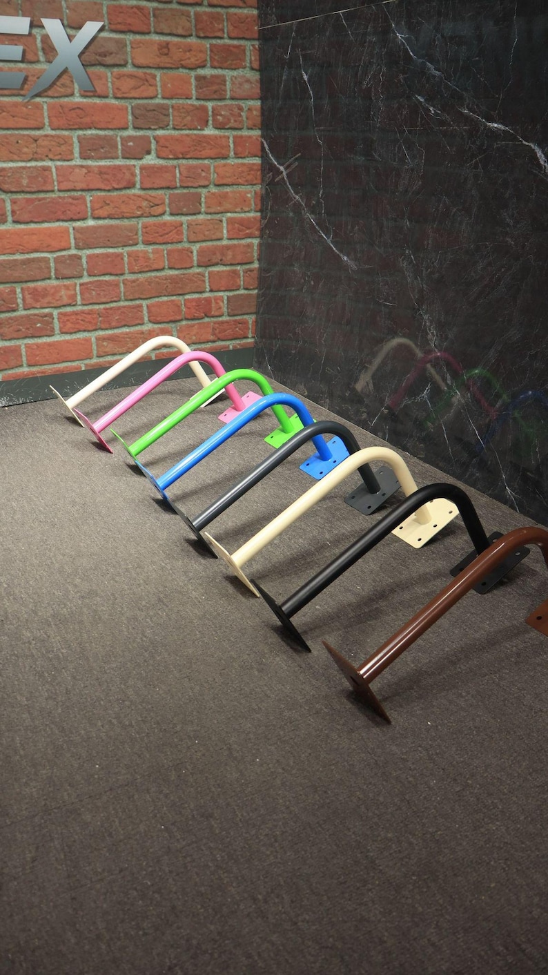 May include: A collection of colorful, curved metal brackets. The brackets are painted in various colors, including pink, green, blue, black, and brown. Each bracket has a flat base for mounting.