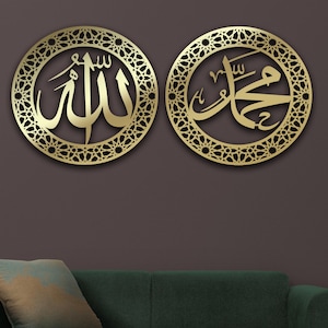 Puede incluir: Dos piezas de decoración de pared de metal de color dorado con intrincados diseños geométricos. La pieza de la izquierda presenta la palabra árabe "Allah" en un marco circular. La pieza de la derecha presenta la frase árabe "Muhammad" en un marco circular.