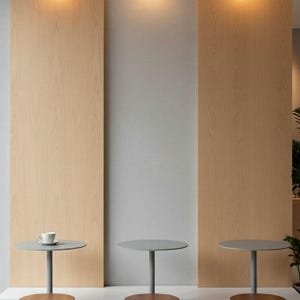 May include: A minimalist interior design featuring three small round tables with gray tops and wooden stools. Each table has a single cup on top. The background includes wooden panels and three round wall-mounted lights.