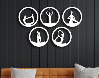 Puede incluir: Cinco piezas de decoración de pared circulares blancas con diferentes poses de yoga en silueta. La decoración está montada en una pared gris oscura.