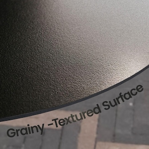 May include: Close-up of a grainy, textured surface. The surface is dark gray and appears to be slightly curved. The words "Grainy - Textured Surface" are printed in a dark font.
