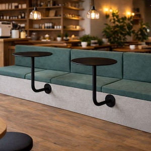 May include: A modern cafe seating area featuring a long, teal-upholstered bench with attached black, round tables. The tables are supported by curved metal arms. The base of the bench is a light gray color. The floor is wood.