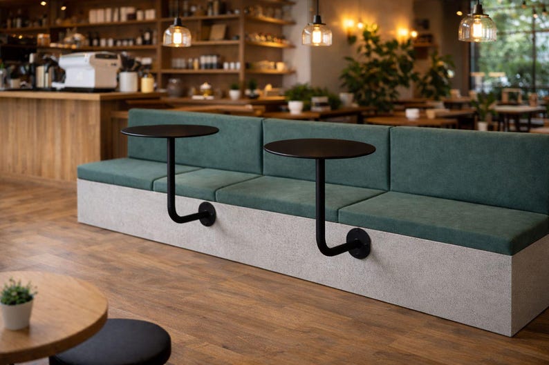 May include: A modern cafe seating area featuring a long, teal-upholstered bench with attached black, round tables. The tables are supported by curved metal arms. The base of the bench is a light gray color. The floor is wood.