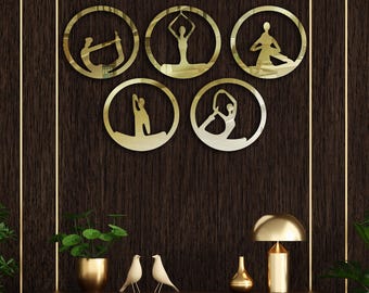 Puede incluir: Cinco espejos de pared redondos de color dorado con siluetas de personas en poses de yoga. Los espejos están dispuestos en semicírculo en una pared de madera oscura.