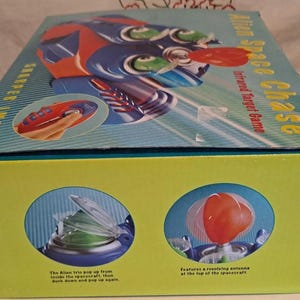 May include: A boxed "Alien Space Chase" infrared target game. The box is primarily yellow with illustrations of the game's spaceship and aliens. The top of the box features the game's name and a spaceship illustration.