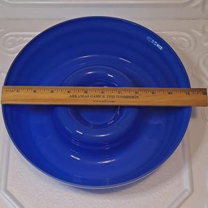 May include: A vibrant blue glass bowl with a concentric design. A wooden ruler, marked in inches, is placed across the bowl. The bowl's diameter is approximately 11 inches.