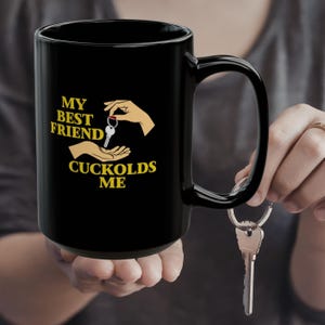 May include: Black ceramic mug with a large handle. The mug features the text "MY BEST FRIEND CUCKOLDS ME" in yellow, along with a graphic of hands and keys. A set of keys hangs from a keyring.