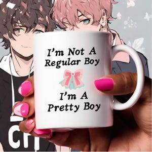 以下が含まれることがあります： 白いセラミック製のマグカップで、黒いグラフィックが「I'm Not A Regular Boy I'm A Pretty Boy」と書いてあり、ピンクのリボンが描かれています。