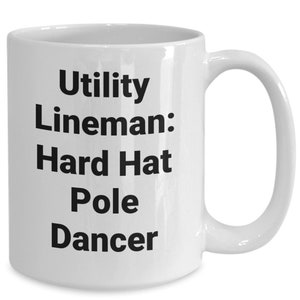 May include: White ceramic coffee mug with black text that reads "Utility Lineman: Hard Hat Pole Dancer".