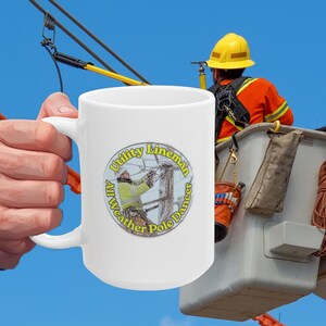 May include: A white ceramic mug featuring a circular graphic of a utility lineman working on a power pole. The text surrounding the image reads Utility Lineman All Weather Pole Dancer in yellow lettering against a clear blue sky background.