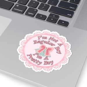 May include: A circular sticker with a pink and white lace-like border. The sticker features the text "I'm Not Regular A Boy I'm A Pretty Boy" in a pink circle, with a bow and bell illustration.