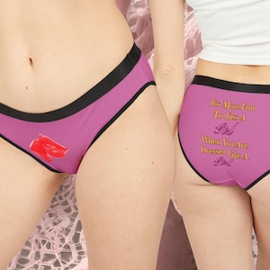 Può includere: Mutandine rosa con bordi neri e grafica di labbra rosse. Il retro della biancheria intima presenta la scritta dorata: "It's More Fun To Kiss A Girl When You Are Dressed Like A Girl".