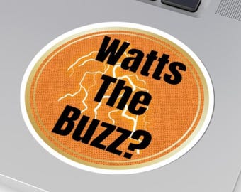 May include: A circular sticker featuring the phrase "Watts The Buzz?" in black lettering, set against an orange backdrop with a white lightning bolt design. The sticker has a gold border and is on a laptop.