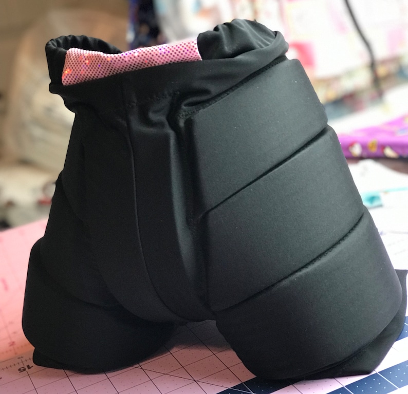 May include: Black padded shorts with a pink sparkly waistband. The shorts have multiple padded sections for protection.