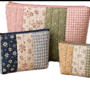 Puede incluir: Un conjunto de tres estuches acolchados de diferentes tamaños, con paneles verticales de estampados florales y cuadros vichy en tonos rosa, verde, azul y amarillo. Cada estuche tiene una cremallera dorada y una correa de muñeca a juego.