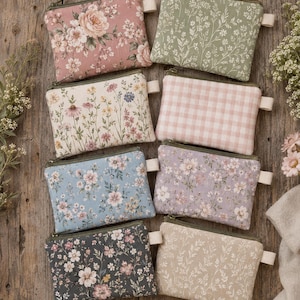 May include: Eight rectangular fabric zipper pouches arranged in two columns. The pouches feature various patterns including pink roses, green foliage, wildflowers on cream, pink gingham, blue floral, lavender floral, dark floral, and beige foliage.
