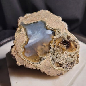 May include: A geode with a light blue and white agate inside. The geode is surrounded by a rough, brown exterior.