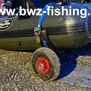 Peut inclure: Un bateau gonflable vert olive avec une garniture noire et une roue attachée. Le bateau porte la marque "FRAZER" sur le côté. Une sangle bleue sécurise le bateau. Le site web "www.bwz-fishing.fr" est visible.