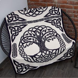 Peut inclure: Une couverture crème avec un motif d'arbre de vie celtique bleu marine foncé. La couverture présente des motifs de nœuds complexes sur les bords et une bordure. La couverture est drapée sur une chaise noire.
