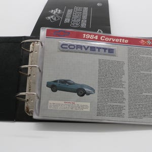 May include: A black binder with a clear plastic sleeve displaying a page about the 1984 Corvette. The page features a blue car illustration, the word "Corvette", and text. A black cover with "The Official Corvette Patch Collection" is visible.