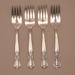 May include: Four silver forks with ornate floral detailing on the handles. The tines are evenly spaced, and the handles have a decorative, elongated shape. The forks are arranged on a neutral background, showcasing their elegant design.