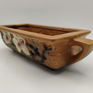 May include: A rectangular, brown ceramic planter with a textured surface and a handle on one end. The planter is decorated with white and purple floral designs and black accents. The interior is a darker brown.