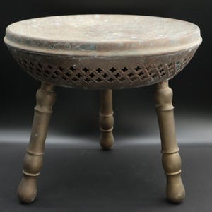 May include: A vintage brass footed plant stand with a round top and three decorative legs. The stand has a pierced, cross-patterned band around the bowl. The metal has a weathered, aged appearance.