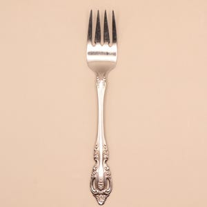 May include: A silver fork with four tines and an ornate handle. The fork is made of a shiny metal and has a decorative pattern on the handle. The tines are evenly spaced and the handle has a detailed design.