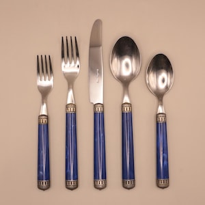 May include: A five-piece silverware set. The set includes two forks, a knife, and two spoons. The handles are a deep blue with a marbled effect, accented with silver-colored metal detailing. The utensils are arranged on a neutral background.