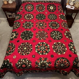 Puede incluir: Una colcha roja con un patrón geométrico en blanco y negro. La colcha está compuesta por muchos octógonos con un diseño floral en el centro. La colcha está sobre una cama.