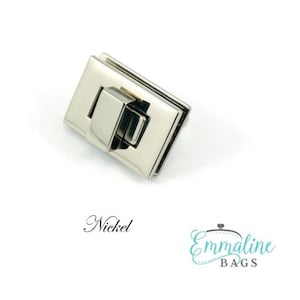 Puede incluir: Cierre de cierre de metal niquelado para bolsos y carteras. El cierre es rectangular y tiene una tapa con bisagras.