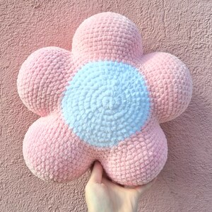 Puede incluir: Una almohada de punto de ganchillo en forma de flor de color rosa y blanco. La almohada tiene un c&iacute;rculo blanco grande en el centro.