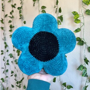 Puede incluir: Una almohada de flores de crochet azul turquesa con un centro negro. La almohada es suave y mullida, y ser&iacute;a una gran adici&oacute;n a cualquier hogar.