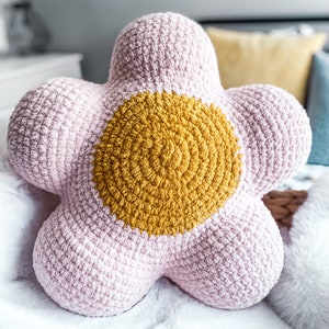 Puede incluir: Una almohada de ganchillo en forma de flor de color rosa y amarillo. La almohada tiene un gran centro amarillo y cinco p&eacute;talos rosas.