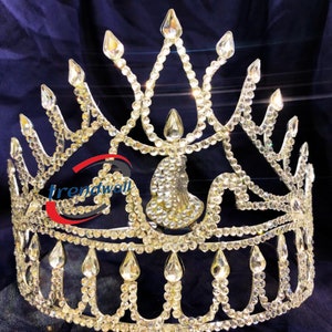 Könnte beinhalten: Eine goldene Krone mit klaren Strasssteinen. Die Krone hat eine spitze Spitze und eine abgerundete Basis. Die Krone ist mit einem floralen Design verziert.