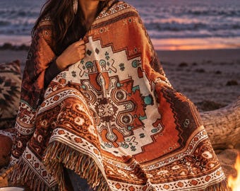 Op de afbeelding: Een geweven plaid met een geometrisch patroon in tinten gebrand oranje, crème en donkerbruin met turquoise accenten. De deken heeft een rand met franjes en toont een centraal symmetrisch ontwerp met ingewikkelde randen.