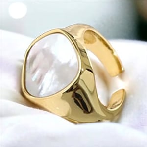 May include: A gold ring with a large, white, iridescent, oval-shaped stone.