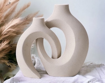 Può includere: Due vasi in ceramica beige con disegni astratti e curvi. I vasi sono annidati l'uno nell'altro, creando un look unico e moderno.