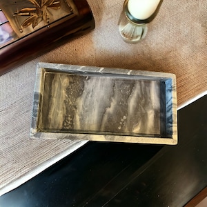 May include: A rectangular tray with a marbled gray and white pattern. The tray has a raised edge and a smooth surface. The tray is made of a solid material and is suitable for holding small items.