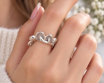 May include: A silver-toned ring featuring a series of small, detailed mushroom caps arranged in a row along the band. The metal has an oxidized finish that highlights the textured gills underneath the mushroom caps and the spotted tops.
