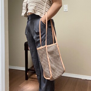 May include: A brown and white houndstooth tote bag with a tan leather trim. The bag has two tan leather straps.