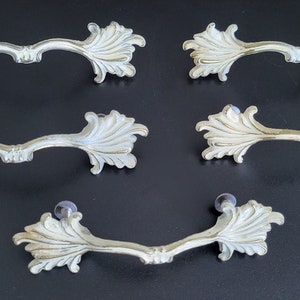 May include: Set of six ornate silver drawer pulls with a leaf design. Each pull has a decorative, stylized leaf on either end.