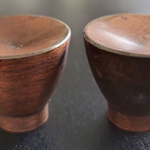 May include: Two small, brown, wooden bowls with a smooth, rounded interior. The bowls have a slightly darker brown rim and a slightly lighter brown base.