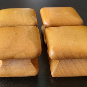 May include: Four wooden drawer pulls with a square top and a rounded bottom. The pulls are a light brown colour.